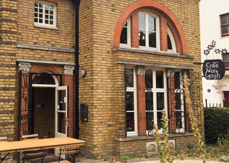 Yellow-brick cafe facade with red-trimmed windows and door.