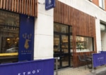 Wooden restaurant facade with black-trimmer windows and doors. Blue banners and signage.