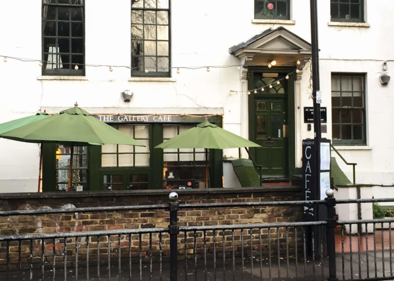 White cafe facade with green-trimmed windows and door. Two parasols outside.