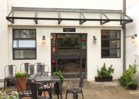 White restaurant facade with windows and door. Tables and chairs outside.