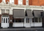 White restaurant facade with black awnings, large windows and two doors.
