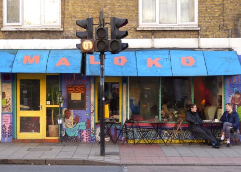 Painted cafe facade with blue awning, large windows and door. Customers sitting outside.