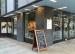 Black restaurant facade with glass door and windows. Sandwich board outside.