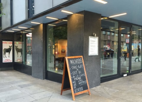 Black restaurant facade with glass door and windows. Sandwich board outside.