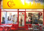 Red bakery facade with glass door and windows. Chairs and tables outside.