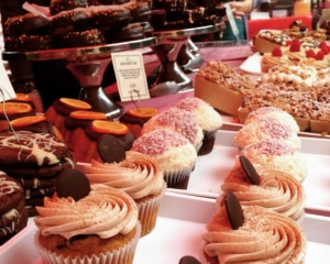 Rows of cupcakes and cookies with cakes and donuts in the background.