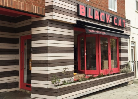 Brown and white restaurant facade with red-trimmed bay window and door.