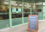 Green restaurant facade with glass door and windows. Sandwich board outside.