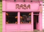 Pink restaurant facade with windows and open door.