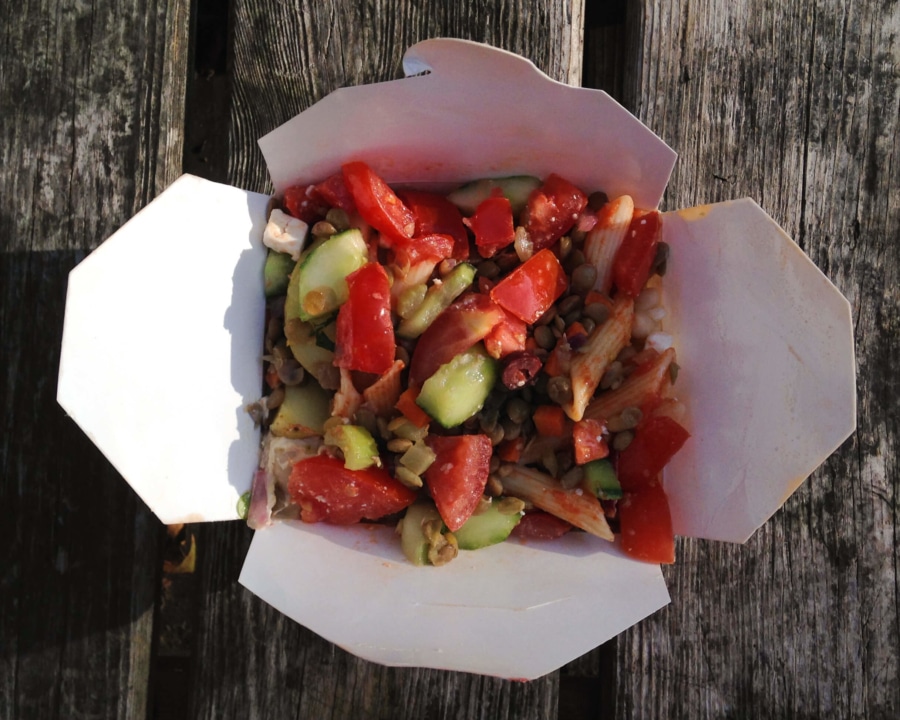 Takeaway carton filled with pasta, lentils and fresh vegetables.