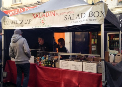 White and red market stall with servers and onlookers.