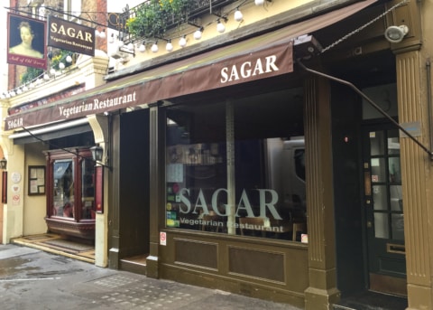 Brown restaurant facade with awning, large windows and door.