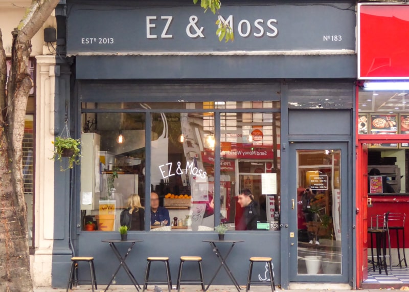 Grey cafe facade with large windows and door. Tables and chairs outside.